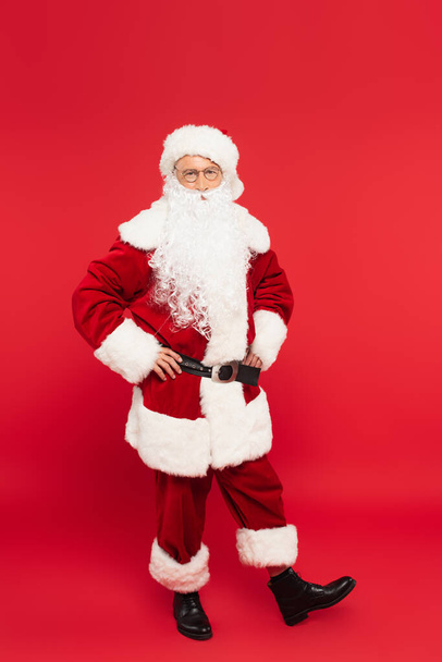 Babbo Natale in costume che si tiene per mano su fianchi su sfondo rosso - Foto, immagini