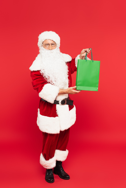 Santa claus in costume holding shopping bag on red background - Foto, Imagen