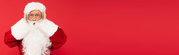 Papai Noel espantado em óculos olhando para câmera isolada em vermelho, banner  - Foto, Imagem