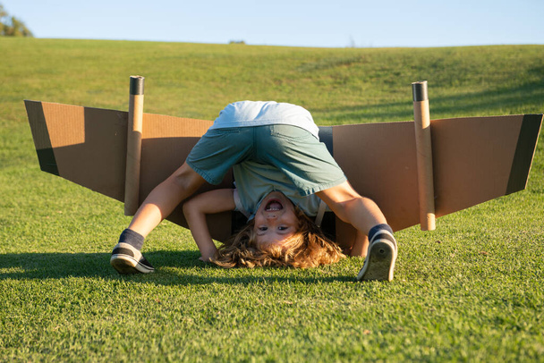Funny child upside down on grass. Childhood imagination, kid dream to adventure travel. Travel and vacation with children. Kids freedom and carefree concept - 写真・画像
