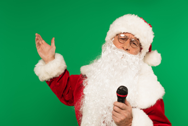 Weihnachtsmann mit Mikrofon zeigt mit Hand isoliert auf grün - Foto, Bild