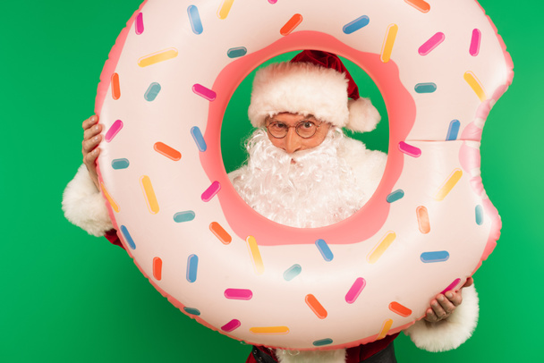 Santa Claus v brýlích drží plavecký kroužek izolovaný na zelené - Fotografie, Obrázek