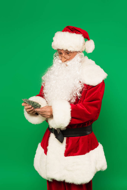 Nadšený Santa Claus drží dolary izolované na zelené - Fotografie, Obrázek