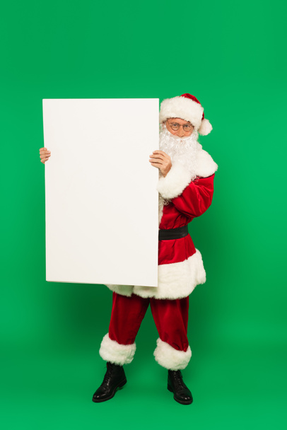Santa claus holding placard with copy space on green background - Foto, Imagen
