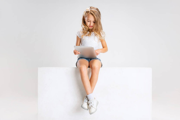 Портрет маленької милої дівчинки в повсякденному одязі, що сидить на великій коробці ізольовано на білому фоні студії. Концепція щасливого дитинства
. - Фото, зображення