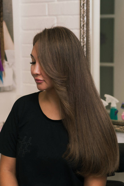 Brunette woman with highlights on long hair in profile in a beauty salon - Fotó, kép