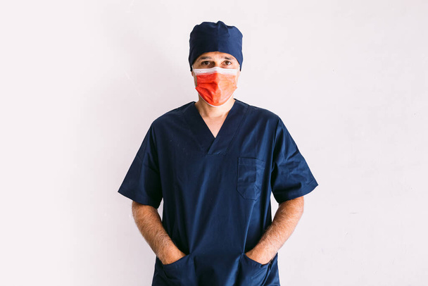 Male nurse, doctor or veterinarian wearing red mask and dark blue uniform in hospital, hands in pockets, smiling. Medicine, hospital and healthcare concept. - Photo, Image