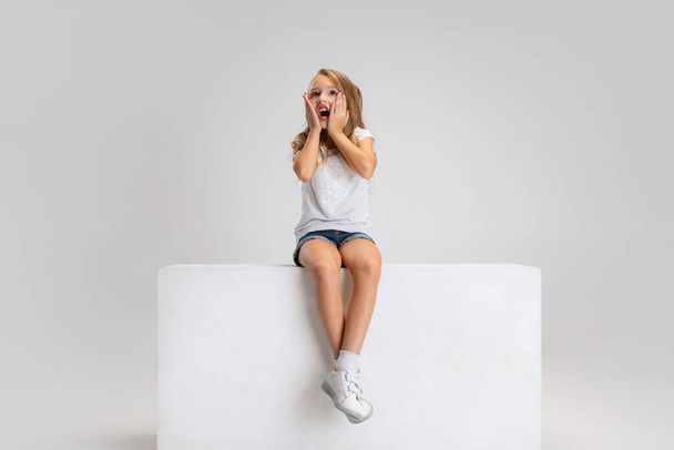 Portrait of little cute girl in casual clothes sitting on big box isolated on white studio background. Happy childhood concept. - Fotoğraf, Görsel