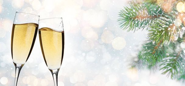 Christmas greeting card with fir tree branch covered by snow, champagne glasses and xmas bokeh background. Holiday card with copy space - Foto, Imagem