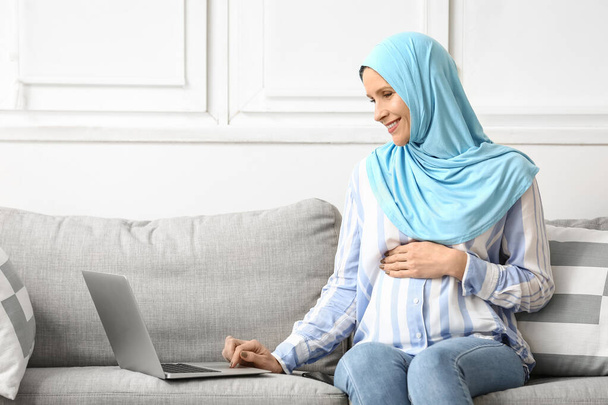 Femme musulmane enceinte travaillant avec un ordinateur portable à la maison - Photo, image