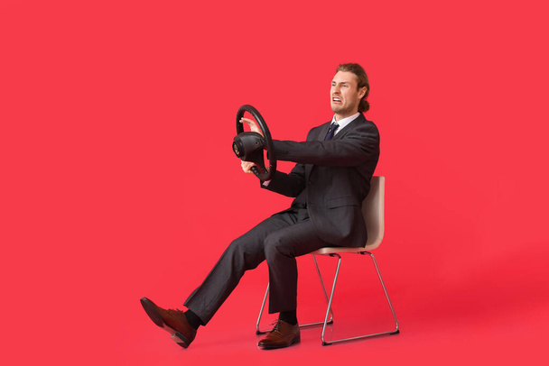Злой молодой бизнесмен с рулем сидит на стуле на цветном фоне - Фото, изображение
