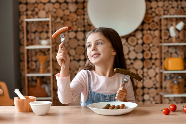 Linda niña con sabrosas salchichas en la cocina - Foto, Imagen