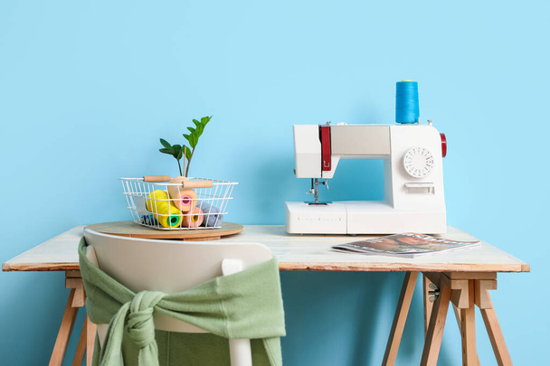 Швейна машина і нитки на столі біля синьої стіни
 - Фото, зображення