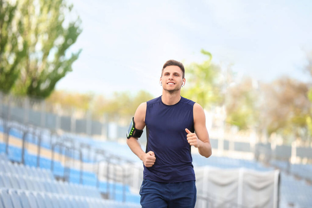 Sporty young man in earphones running at stadium - Fotografie, Obrázek