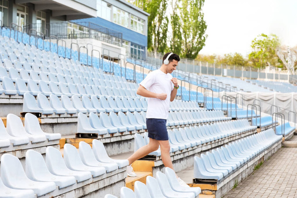Sporty young man in headphones running downstairs at stadium - Fotoğraf, Görsel