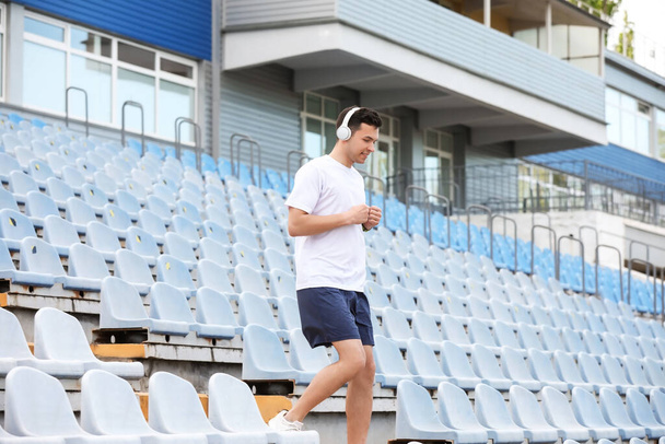 Sportlicher junger Mann mit Kopfhörern läuft im Stadion die Treppe hinunter - Foto, Bild