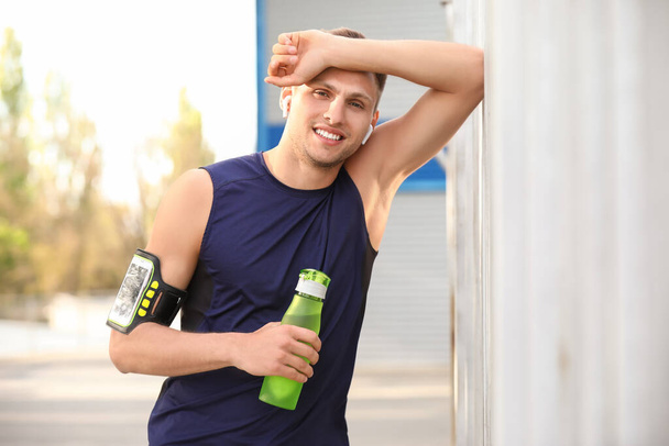 Tired young man with bottle of water after training at stadium - Foto, imagen