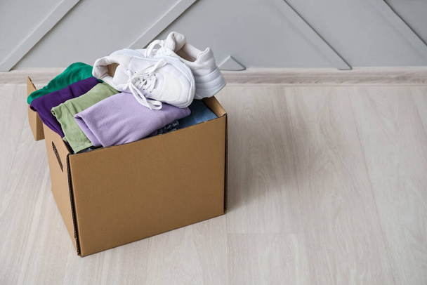 Caixa de guarda-roupa com roupas e sapatos no chão de madeira perto da parede leve - Foto, Imagem