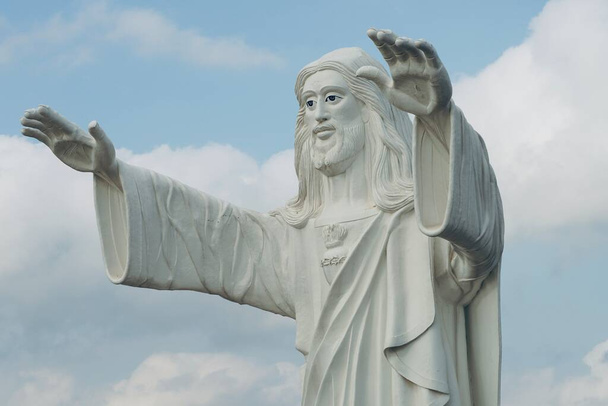 Posąg Jezusa stojący i błogosławiony obiema rękami na tle niebieskiego nieba. - Zdjęcie, obraz