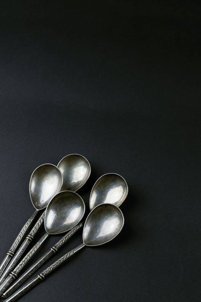 п'ять старовинних срібних чайних ложок на чорному фоні
 - Фото, зображення