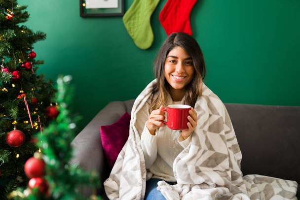 Gorgeous woman with a santa hat enjoying a cup of hot chocolate at home during a chilly winter morning - Foto, afbeelding