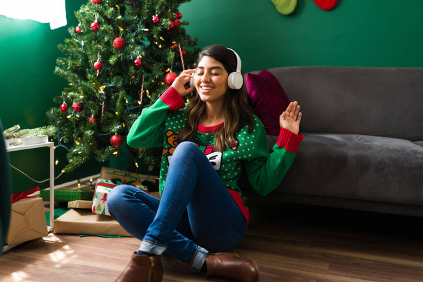 Élvezem a zenét. Vidám fiatal nő hallgatja kedvenc karácsonyi dalát vezeték nélküli fejhallgatóval  - Fotó, kép