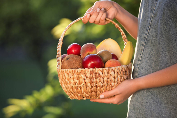 Жінка тримає плетений кошик зі свіжими фруктами на відкритому повітрі, крупним планом
 - Фото, зображення
