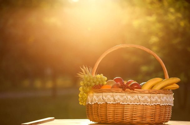 テーブルの上に新鮮な果物とウィッカーバスケット屋外 - 写真・画像