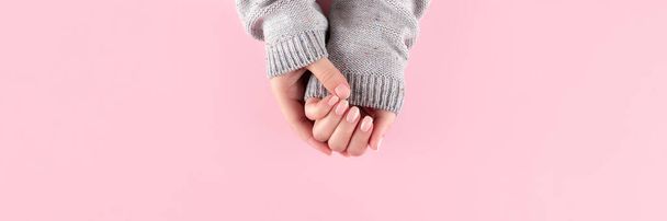 Handen in trui met naakte nagels op roze achtergrond - Foto, afbeelding