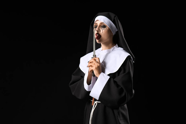 vrouw gekleed voor Halloween als non met mes op donkere achtergrond - Foto, afbeelding