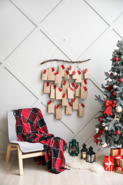 Pohodlné křeslo s kostkovanými kostkami, vánoční stromeček a adventní kalendář na světlé stěně v pokoji - Fotografie, Obrázek