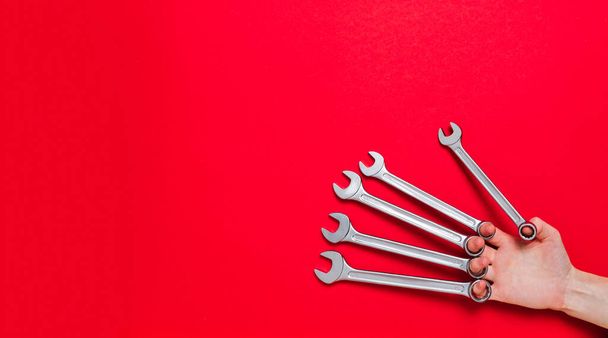 Hand fingers hold a set of wrenches different size on a red background. Banner with tools and copy space with industrial holiday concept. Business card or certificate of auto service. Instrument shop. - Foto, Bild