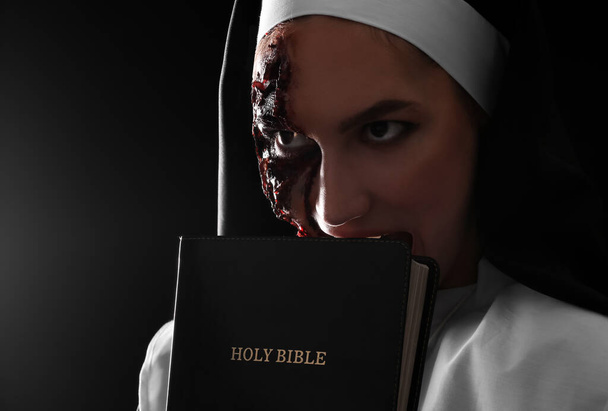 Woman dressed for Halloween as nun with Bible on dark background - Fotoğraf, Görsel