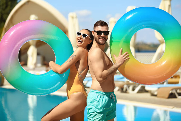 Νεαρό ζευγάρι με φουσκωτά δαχτυλίδια κοντά στην πισίνα - Φωτογραφία, εικόνα