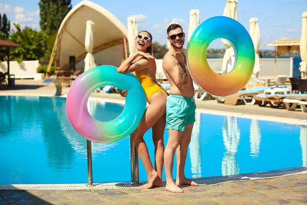 Young couple with inflatable rings near swimming pool - Photo, Image