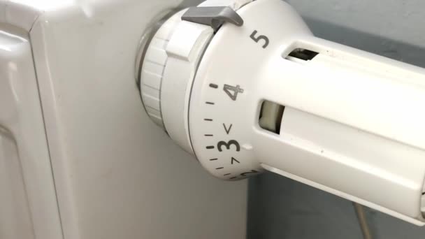 Ręka mężczyzny skręca białą rączkę termostatu na kaloryferze - Materiał filmowy, wideo