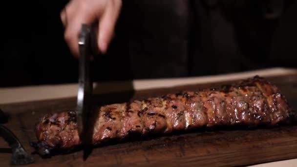 Butcher chop juicy grilled pork ribs with a hatchet on a wooden tray in a dark room. Slow motion - Footage, Video