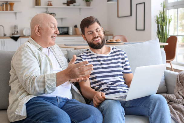 Ο άνθρωπος και ο πατέρας του με το laptop βίντεο κουβεντιάζοντας στο σπίτι - Φωτογραφία, εικόνα