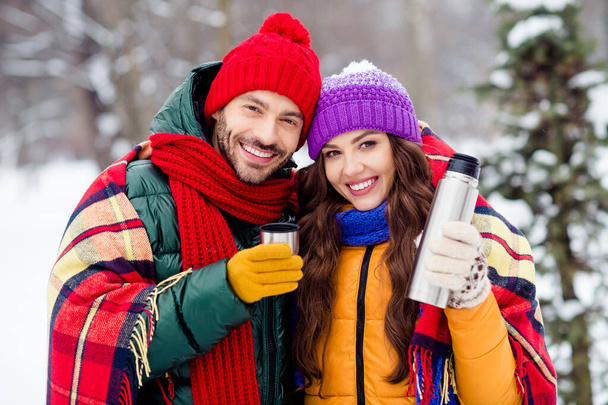 Photo of cute charming marriage couple wear windbreakers drinking hot coffee covering blanket walking snowy weather outside park - Foto, afbeelding
