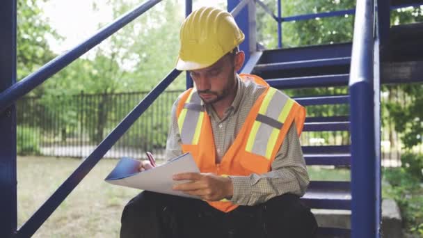Civil engineer in helmet and safety vest taking notes in notepad - Footage, Video