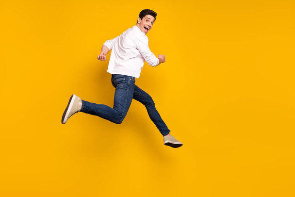 Full length profile photo of cool brunet young guy run wear shirt jeans sneakers isolated on yellow background - Foto, afbeelding