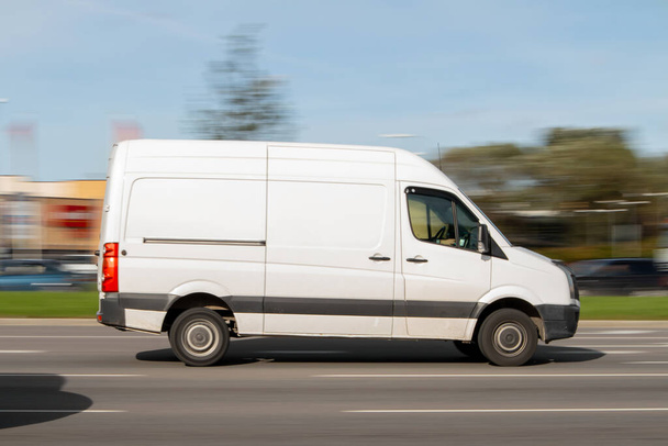 Ein weißer Lieferwagen fährt schnell die Straße hinunter. Nutzfahrzeuge für kleine Lasten, Paketzustellung. Bewegungsunschärfe - Foto, Bild
