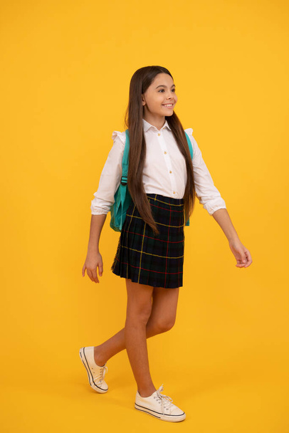 feliz adolescente chica en la escuela uniforme completo longitud en amarillo fondo haciendo paso adelante, escuela. - Foto, imagen