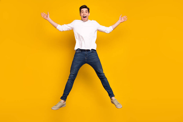 Full body photo of impressed brunet young guy jump wear shirt jeans sneakers isolated on yellow background - Фото, зображення