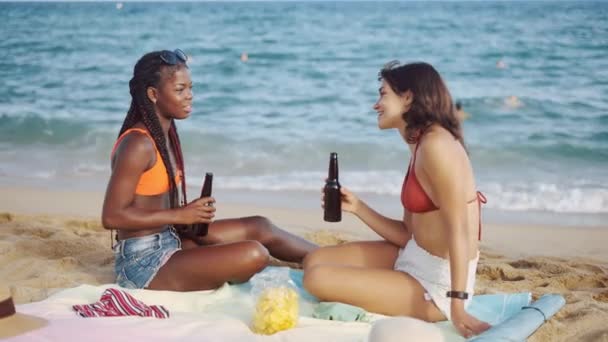 Mejores amigas en la playa de arena sentado con bebidas - Metraje, vídeo