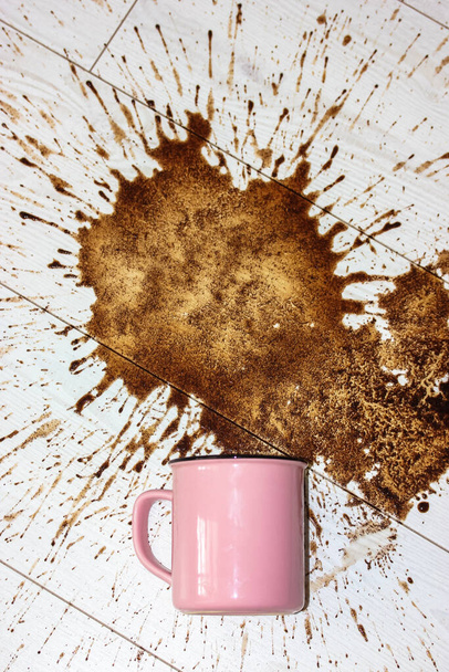 Una taza de cerámica rosa, taza cayó sobre un suelo de parquet de madera blanca y dejó una gran mancha en ella. Derramó café por la mañana. Un montón de café caliente bebida salpicaduras marrones volando en diferentes direcciones llanamente.  - Foto, Imagen