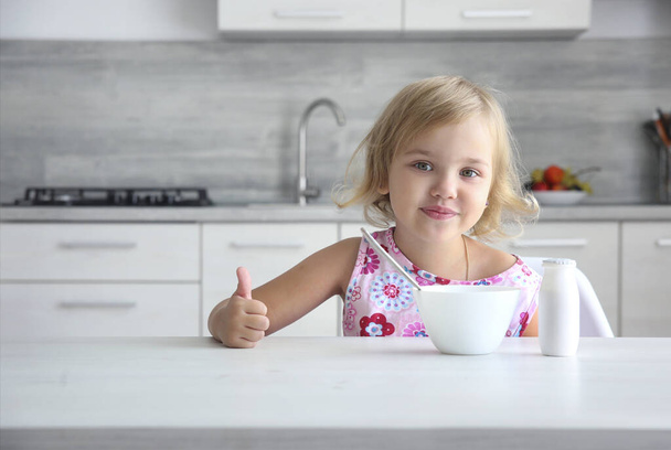 Caucasian child girl sitting at table with empty space. Kid has a lunch. Little toddler has a meal at the kitchen. Food advertisement design image. - Foto, Imagen