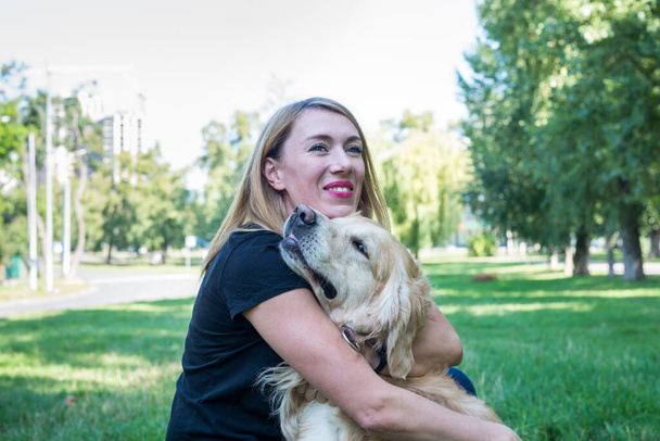 Blonde woman hugs retriever dog outdoors - Foto, imagen