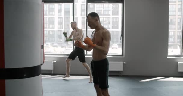 Due combattenti sono calci sacchi da boxe in palestra al rallentatore, combattenti di arti marziali miste si allenano, 4k 120fps Prores HQ - Filmati, video