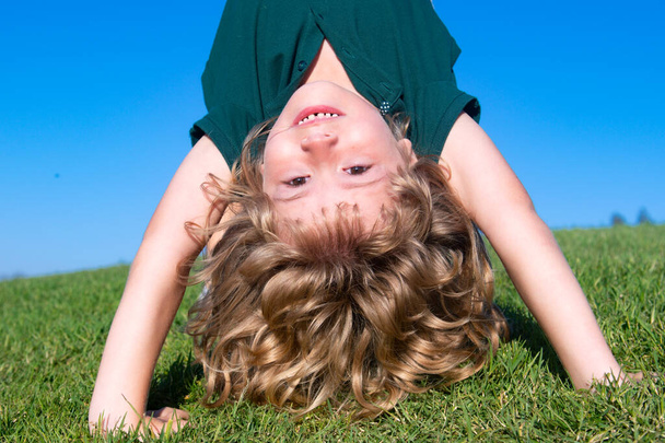 Portrait of a happy smiling child boy playing upside down on grass field outdoor. Laughing child. Expressive facial expressions. - Photo, Image
